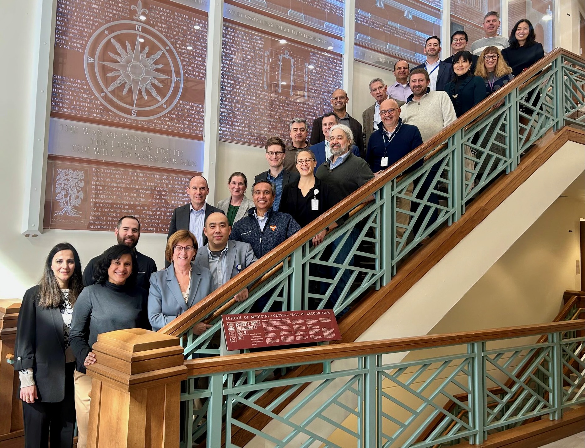 Group of faculty and staff posing on a staircase beside the School of Medicine Crystal Wall of Recognition