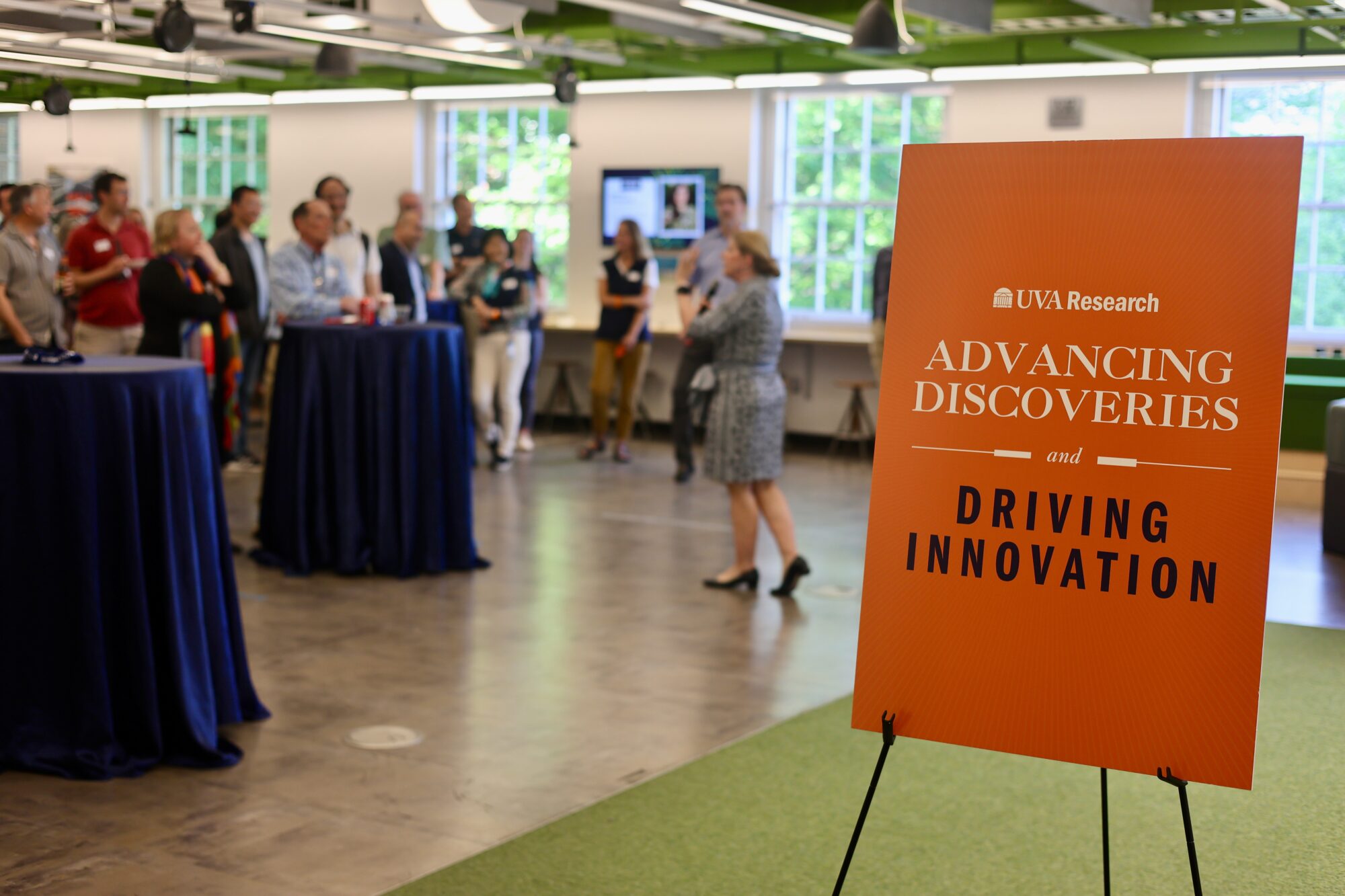 UVA Research event sign reading "Advancing Discoveries and Driving Innovation" with attendees gathered in the background